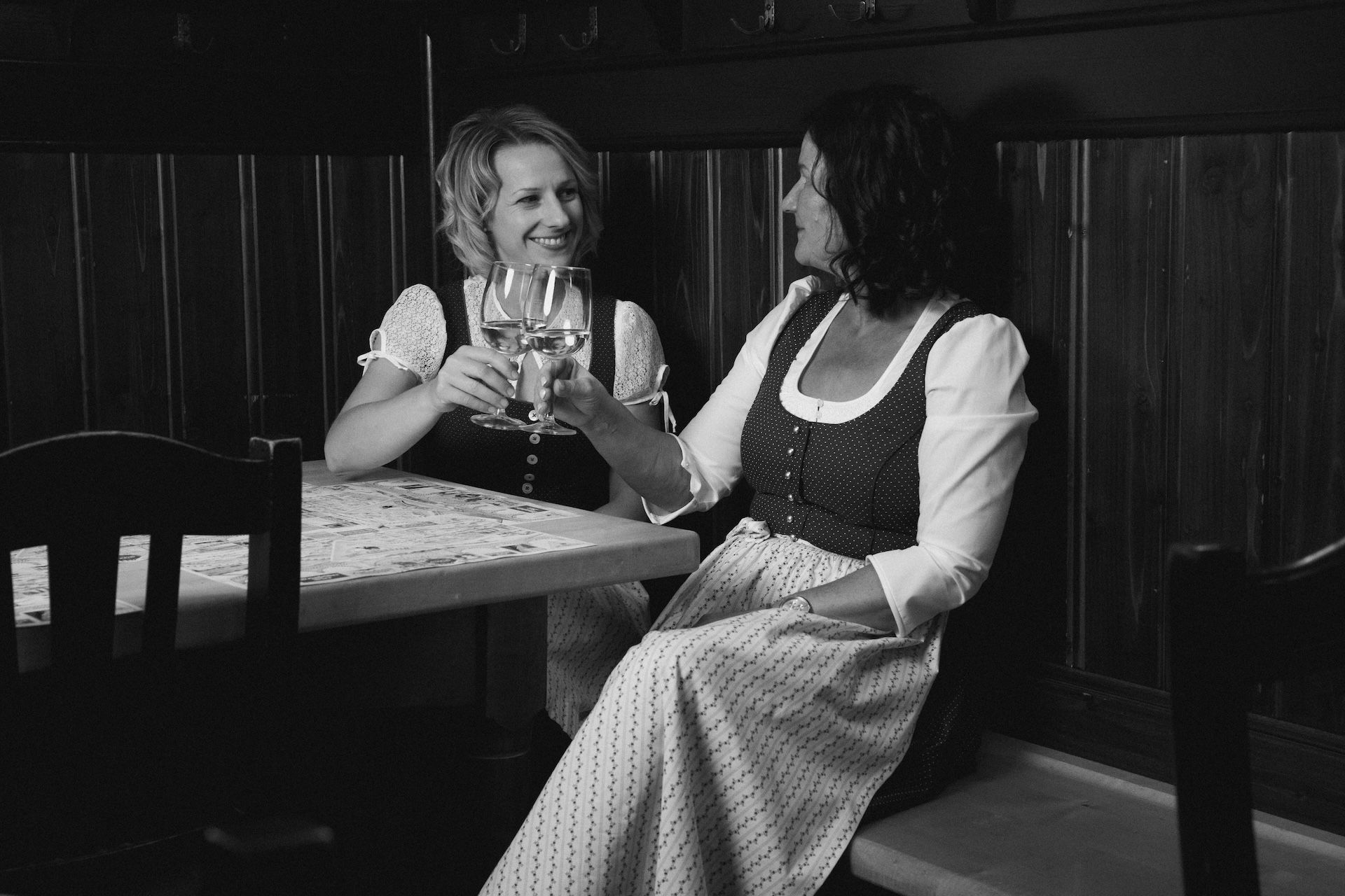 Zwei Frauen in Tracht sitzen an einem Tisch mit einem Glas Wein